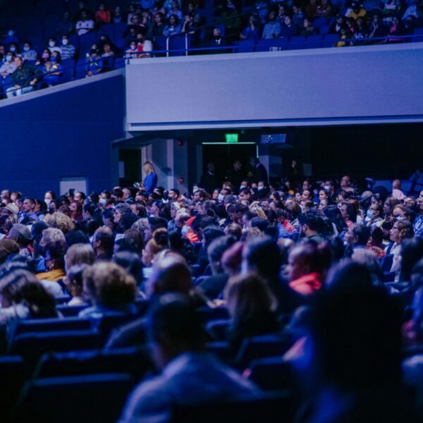 A crowded conference hall with diverse audience attentively listening to a speaker.
