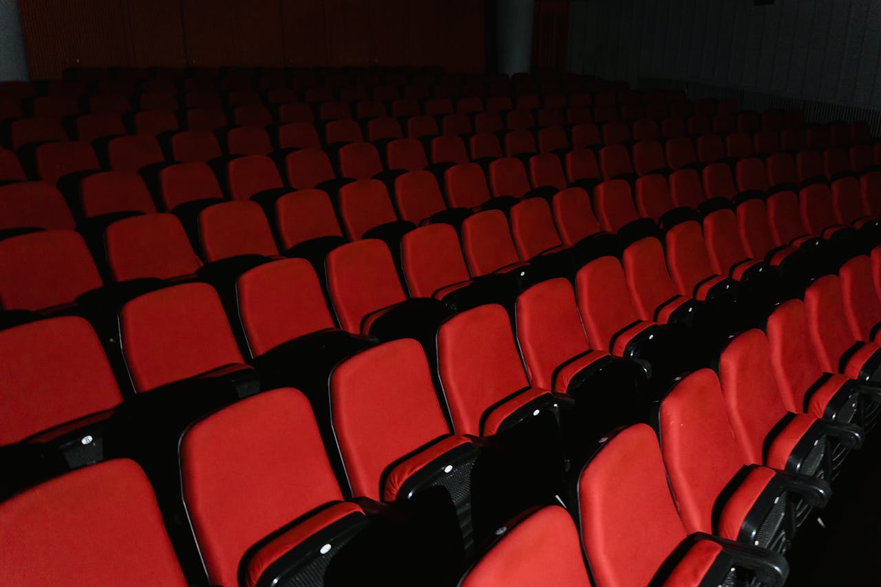 our-story-02 A view of empty red theater seats arranged in rows inside a cinema hall.